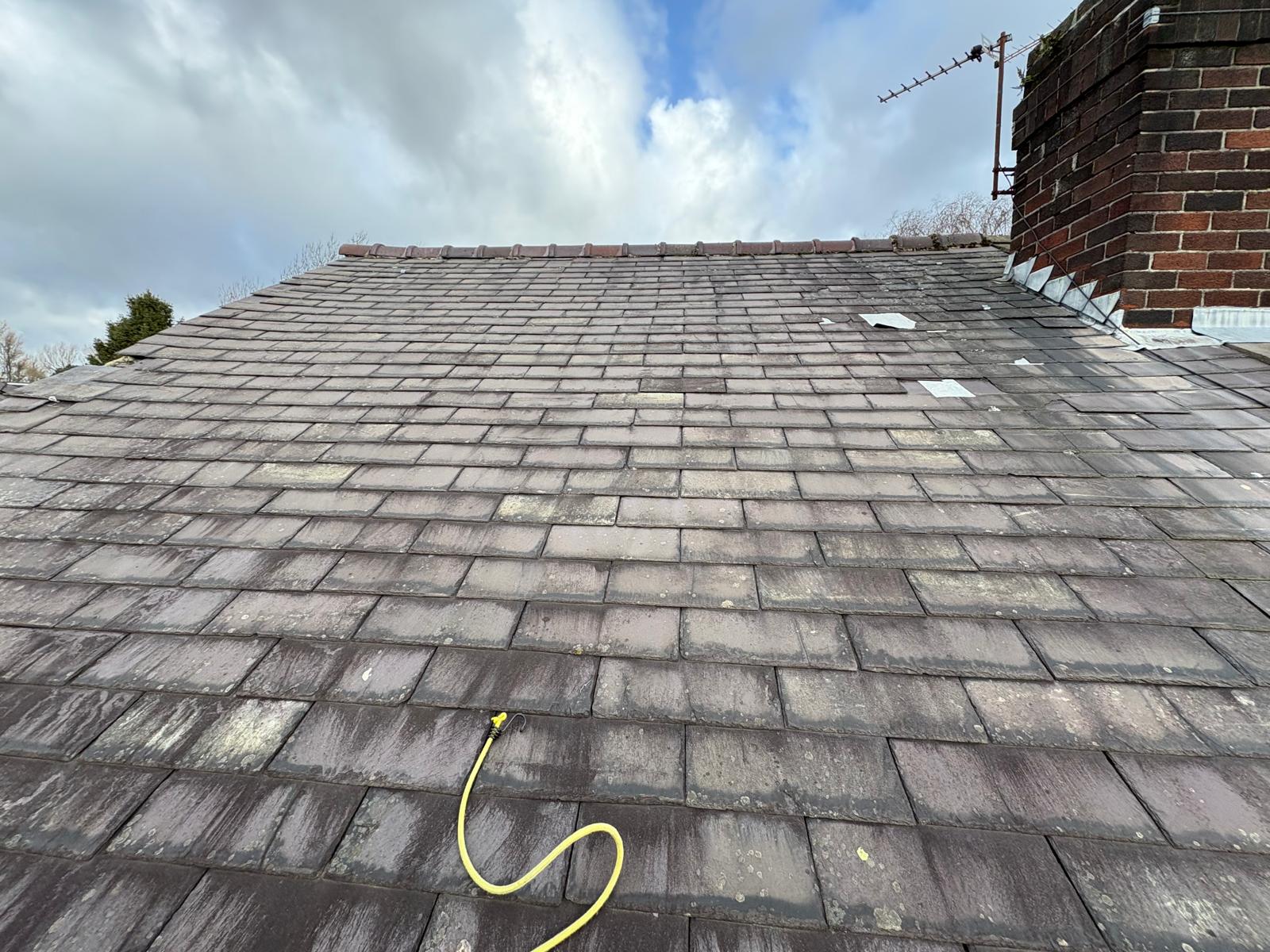 Weathered grey slates on a pitched slope beside a brick chimney